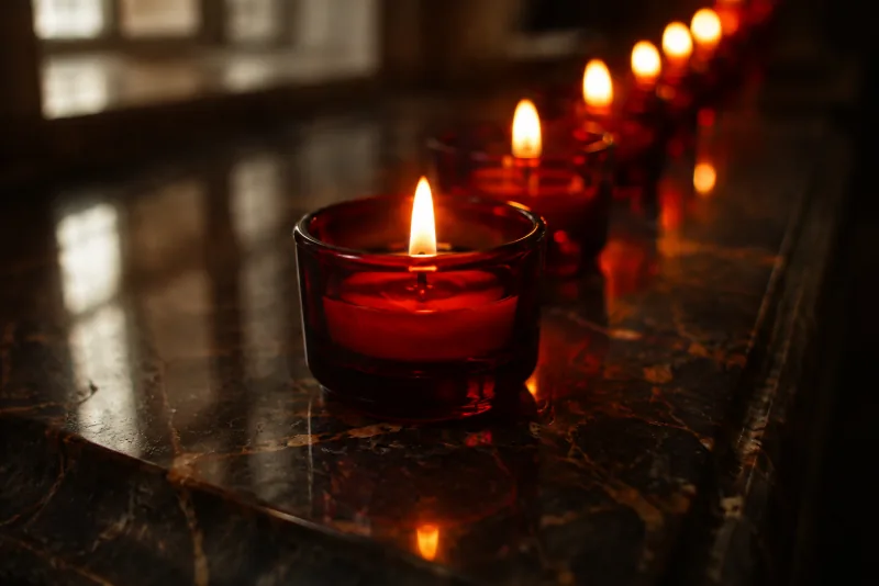 Red glass votive candles glow in a row and reflect on polished dark stone.