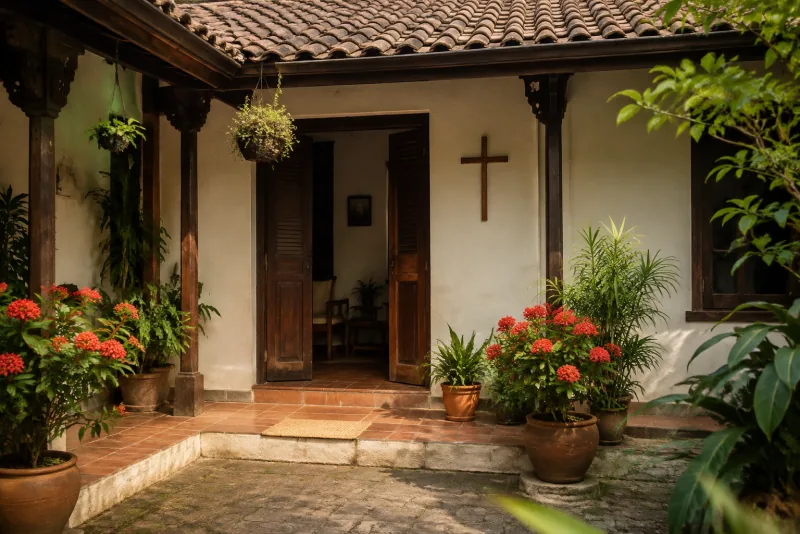 Salib kayu menghiasi dinding rumah dengan pintu terbuka dan pot bunga di halaman.